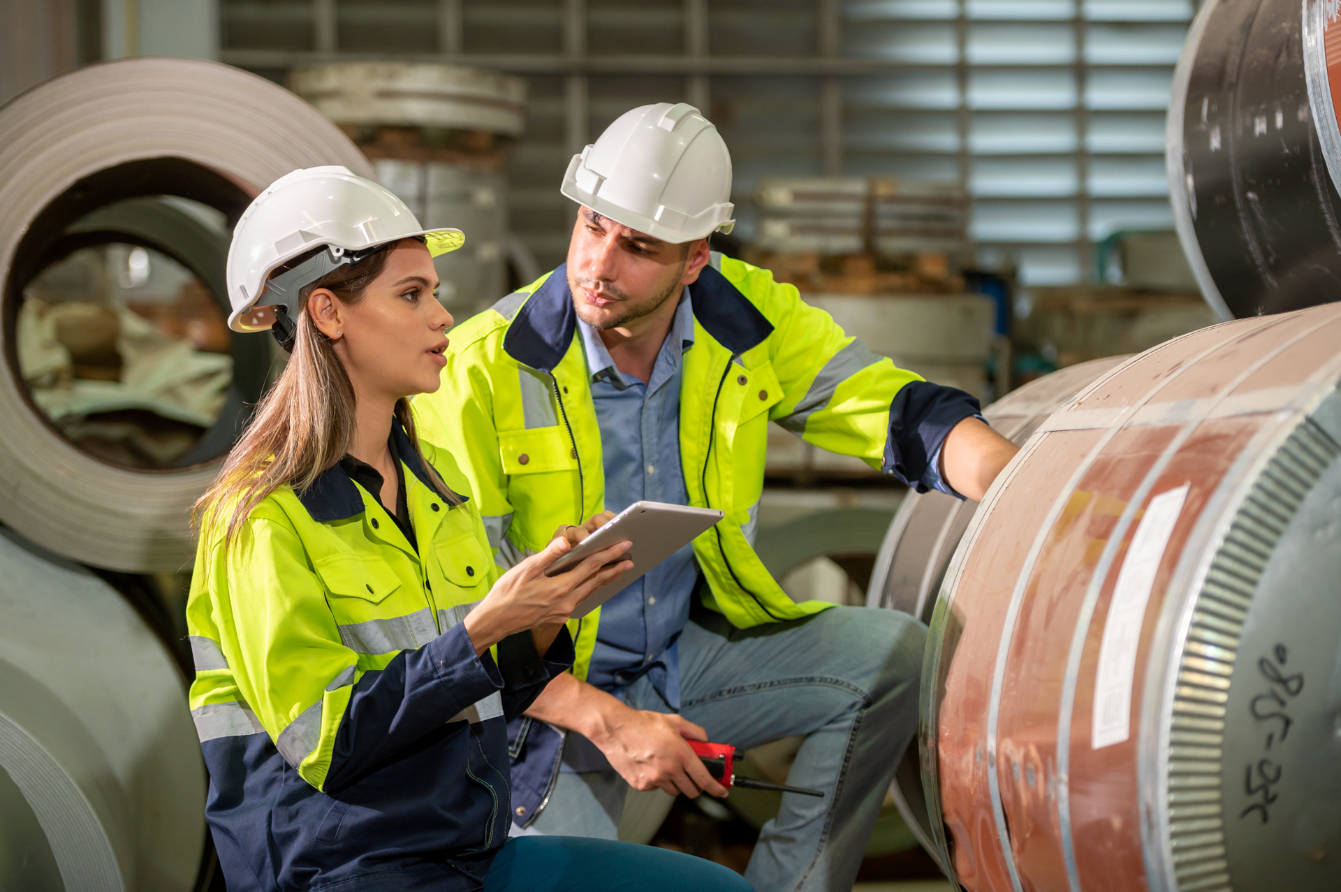 A female worker in PPE holding a tablet with DeepHow training content talking with a male employee in PPE about the content.