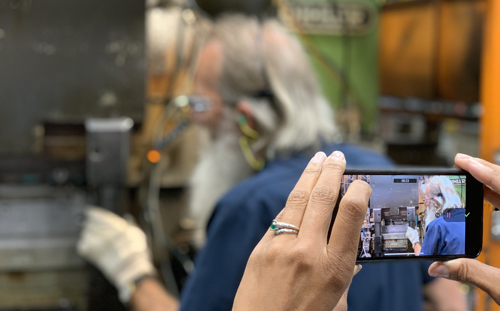 A female worker using the DeepHow app on a phone to film another worker operating a machine.