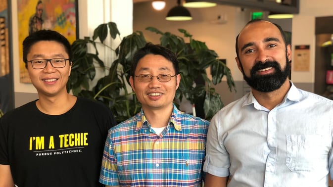 DeepHow founders Wei-Liang Kao, Sam Zheng, and Patrik Matos standing in an office building.
